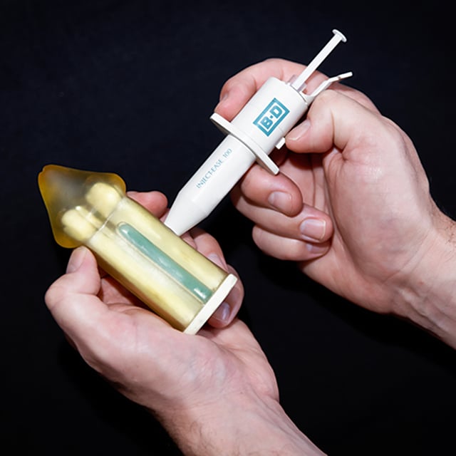 Demonstration of an auto injector positioned perpendicular and halfway down the shaft, highlighting the spring-loaded button. 